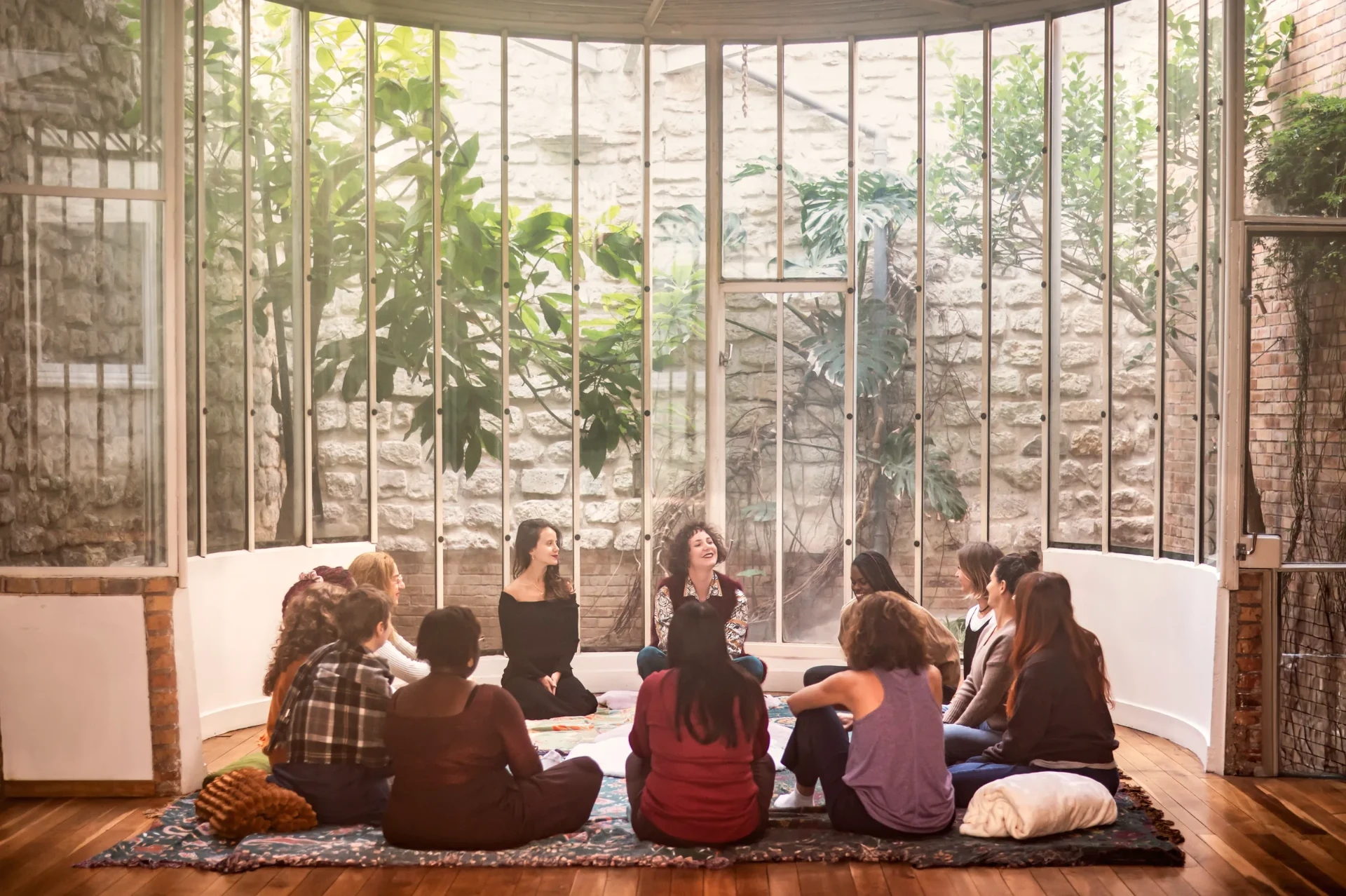 a circle of participants sitting on rugs beneath the glass roof